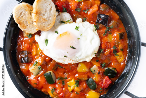 Vegetable pisto manchego with tomatoes, zucchini, peppers, onions,eggplant and egg, served in frying pan isolated on white background. Close up