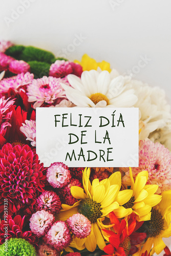 vertical photo of a bright beautiful bouquet of multicolored flowers, white greeting card with the inscription Happy Mother's Day in Spanish, mother's day concept.