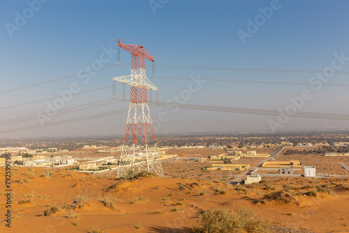 Desert landscape with Al Digdaga village in Ras al Khaimah, UAE, golden desert dunes, with high voltage transmission tower and residential buildings on the horizon.