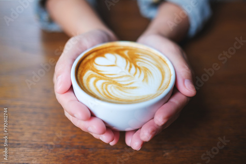Closeup image of a woman holding a cup of hot coffee with latte art