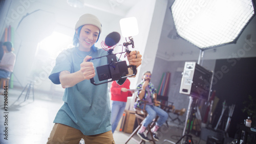 Young Caucasian Female Videographer With Blue Hair, Wearing A Beanie, Captures Content In A Studio, Surrounded By Professional Lighting Equipment And Team Members Engaged In A Creative Production.
