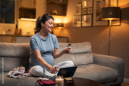 A happy pregnant woman typing in her credit card number on the tablet for online shopping