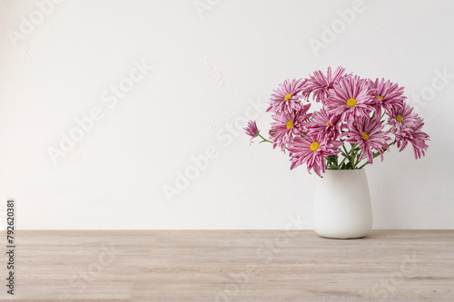 Minimalist floral product background with empty copy space, wooden beige neutral table, white concrete wall surface, vase with pink daisy flowers bouquet, aesthetic home interior decor mockup