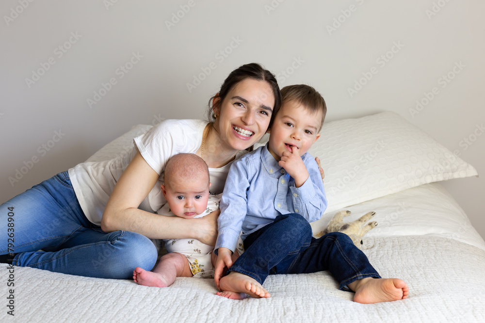Young mother holding her adorable toddler boy and baby girl while sitting on bed in casual clothes, Quebec City, Quebec, Canada Young mother holding her adorable toddler boy and baby girl while sitting on bed in casual clothes, Quebec City, Quebec, Canada