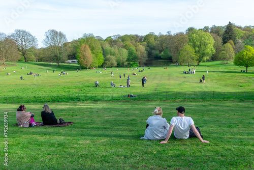 London. UK- 04.14.2023. Crowd of people relaxing and enjoying a day out on the green grass field of a park on a beautiful warm sunny Spring day.