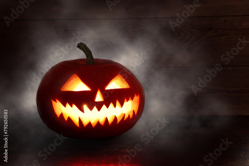 Spooky Halloween pumpkin, Jack O Lantern, with an evil face and eyes on a wooden table with a misty gray background.