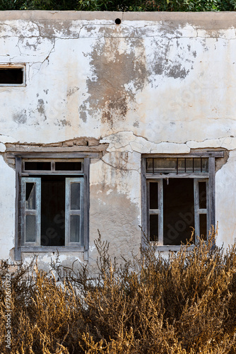 Neglected building facade with broken windows and blue window shutters in Al Jazirah Al Hamra haunted town in Ras Al Khaimah, United Arab Emirates.