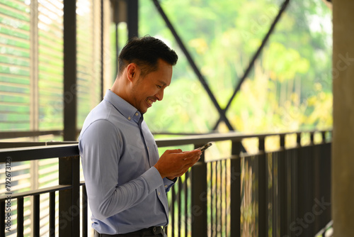 Smiling businessman using smartphone standing at the walkway inside a building