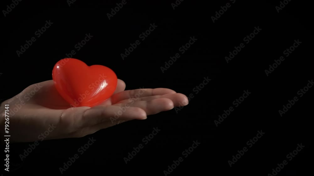 Woman and child hold red heart indoor. A view of woman and child palms holding red heart against black background.