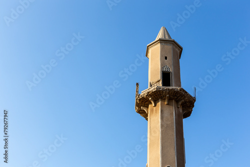 Old destroyed sandstone minaret of a mosque against crystal blue sky background in Al Jazirah Al Hamra haunted town in United Arab Emirates.