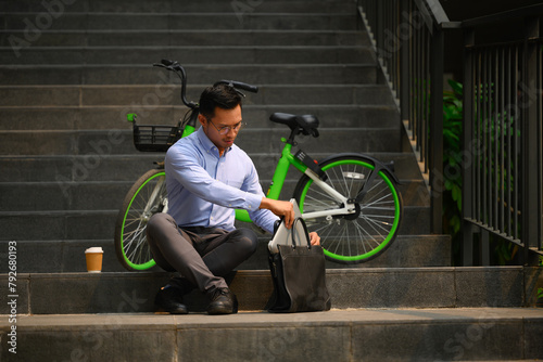 Shot of businessman with briefcase sitting on stairs in the city near his bicycle