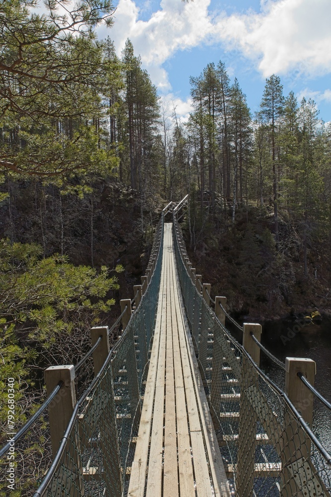 Wooden suspension bridge over river in cloudy spring weather at Kitkakoski rapids, Oulanka National Park, Kuusamo, Finland.