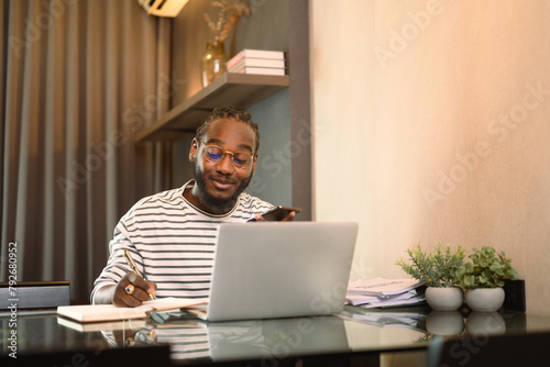 Smiling male entrepreneur working with laptop and making note at desk in living room