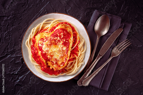 Chicken Parmesan, Italian pasta dish. Breaded chicken breast with cheese and spaghetti with tomato sauce, overhead flat lay shot on a black slate background