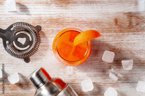 Orange cocktail and a shaker, with ice, overhead flat lay shot on a wooden background with copy space