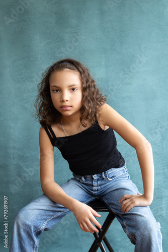 Vertical view of cute mixed race nine-year old girl sitting on stool with serious attitude and expression