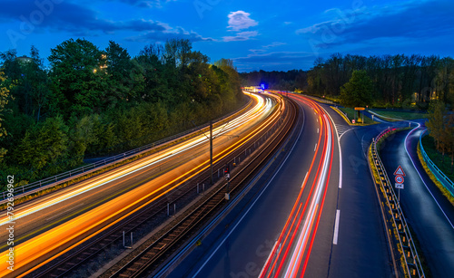 Blue hour panorama of “B54” expressway in the south of Dortmund in the Ruhr area (Germany). Curve with four lanes and double-track tram route in blue hour. Colorful light traces from train and cars. photo