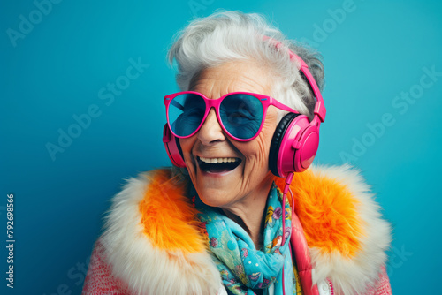 Happy elderly lady in sunglasses laughs while listening to music on blue background