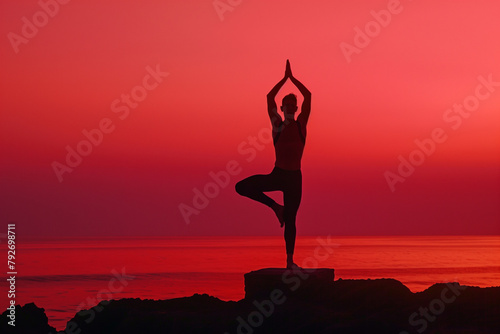 Silhouette of a man doing a yoga tree pose an the sea against a sunset sky