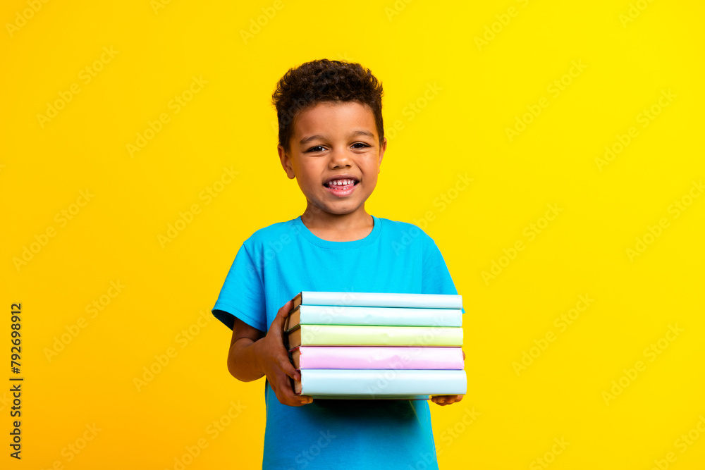 Photo of intelligent child with curly hair dressed blue stylish t-shirt holding book do homework isolated on vibrant yellow background Photo of intelligent child with curly hair dressed blue stylish t-shirt holding book do homework isolated on vibrant yellow background