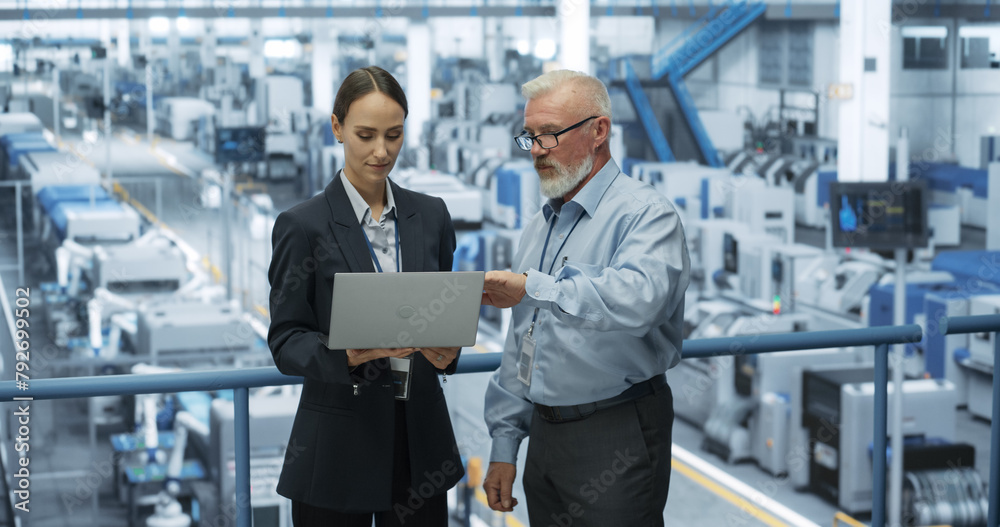 Experienced Male and Female Engineers Standing on a Platform at a Modern Industrial Factory, Using Laptop Computer and Discussing Production of Modern Electronics for Artificial Intelligence Machines Experienced Male and Female Engineers Standing on a Platform at a Modern Industrial Factory, Using Laptop Computer and Discussing Production of Modern Electronics for Artificial Intelligence Machines
