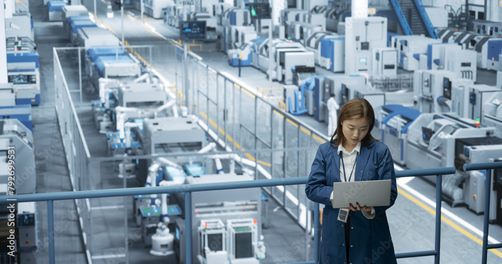 Japanese Factory Specialist Working on Laptop at a Futuristic Industrial Manufacture with Autonomous AI Robots. Project Manager Monitoring Data on a Computer, Checking Reports and Planning Research Japanese Factory Specialist Working on Laptop at a Futuristic Industrial Manufacture with Autonomous AI Robots. Project Manager Monitoring Data on a Computer, Checking Reports and Planning Research