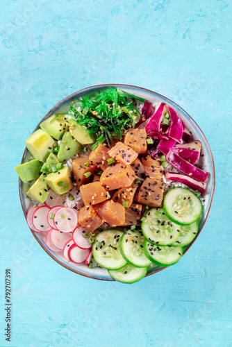 Tuna poke bowl with avocado, cucumbers, wakame, radish, and purple cabbage, a healthy Hawaiian dish with rice, shot from the top on a blue background