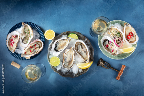 Oysters on ice, with various toppings and white wine, overhead flat lay shot on a blue slate background