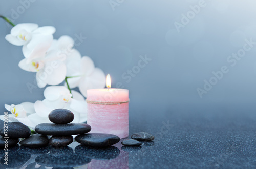 Spa background with white orchid , candle and zen black stones on gray.