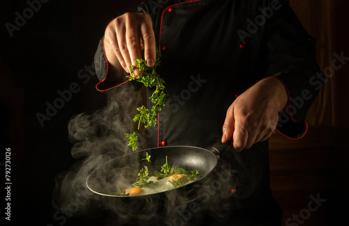 Schilderij op canvas The chef throws fresh aromatic parsley into the scrambled eggs in a hot frying pan with his hand