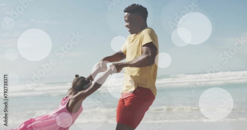 Image of light spots over african american father and daughter playing on beach