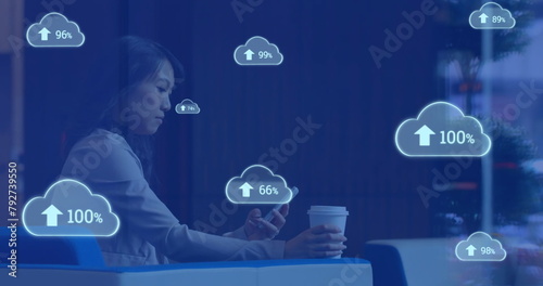 Image of cloud symbols uploading data over asian businesswoman using smartphone at cafe