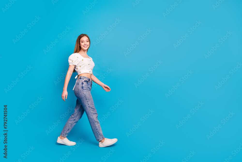 Full length profile portrait of lovely girl walk empty space ad wear top isolated on blue color background