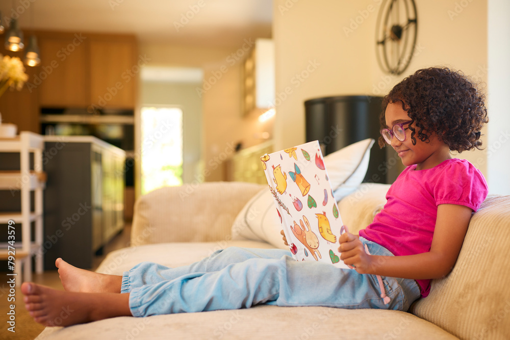 Girl Wearing Glasses At Home Sitting On Sofa Reading A Story Together Girl Wearing Glasses At Home Sitting On Sofa Reading A Story Together