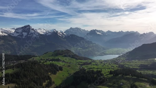 The serene charm of Amden and Arvenbüel, Switzerland, through captivating drone footage showcasing green mountains, charming villagewith tall trees, and sky painted with wispy white clouds. photo