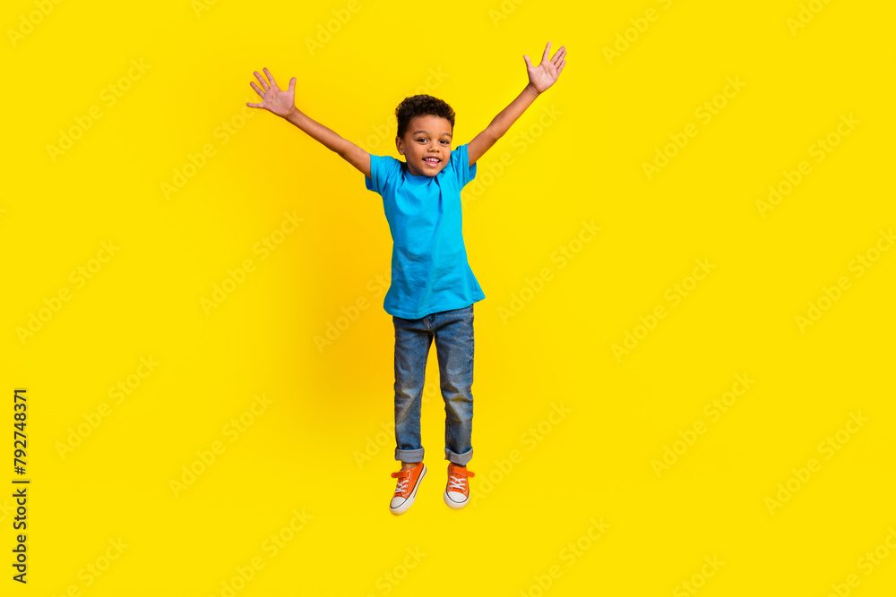 Full body photo of positive cute small child dressed blue t-shirt jeans flying raising arms up isolated on vibrant yellow background Full body photo of positive cute small child dressed blue t-shirt jeans flying raising arms up isolated on vibrant yellow background
