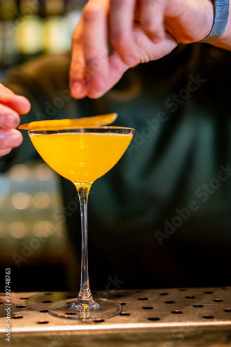 A skilled bartender garnishing a bright yellow cocktail in a martini glass, showcasing the elegance of mixology