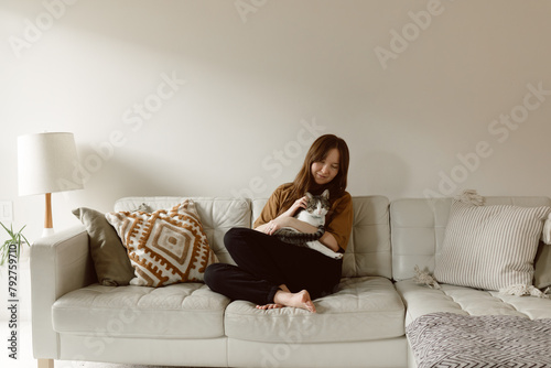 Woman cuddles with cat on couch in front of blank wall