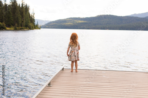 Redhead girl standing on a dock overlooking a serene lake.