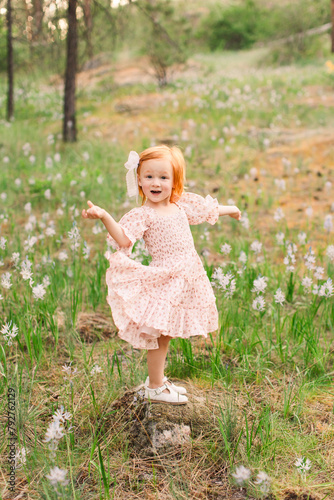 Smiling red haired girl in a floral dress among spring wildflowe photo
