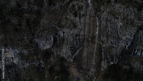 Rising drone clip of high mountain waterfall showing steep rock face and water's edge at base of cliff photo