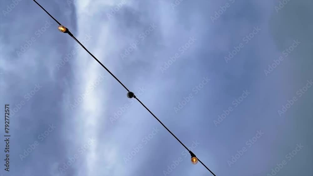 Bulbs on a light string with a cloudscape time lapse in the background - looking up Bulbs on a light string with a cloudscape time lapse in the background - looking up