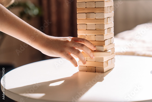 A child slides a wooden block of Jenga game on a white table under sunlight. photo