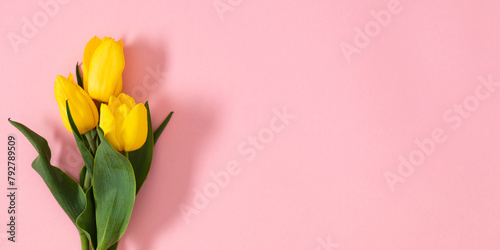 Festive pink background with yellow tulips. Bouquet of yellow tulip flowers on pink table background. Top view, flat lay.