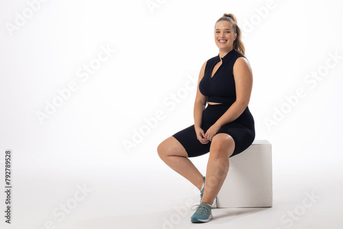 A young Caucasian plus-size model sits on white block with a white background, copy space