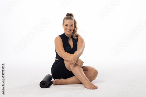 Young Caucasian plus-size model sits on white background, smiling at camera, copy space