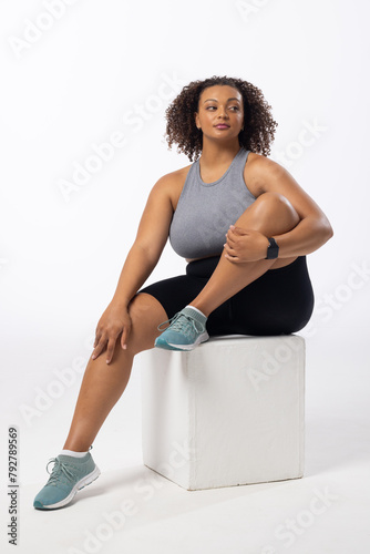 Biracial plus size model with curly hair holds leg on white background, copy space