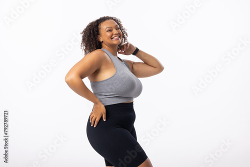 Biracial young female plus size model stands on white background, hand on hip, copy space