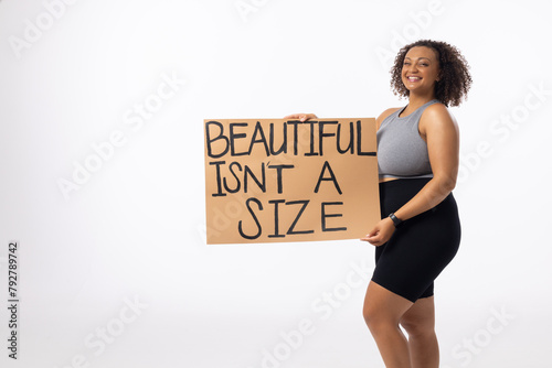 A biracial plus size model holds body positivity poster on a white background, copy space