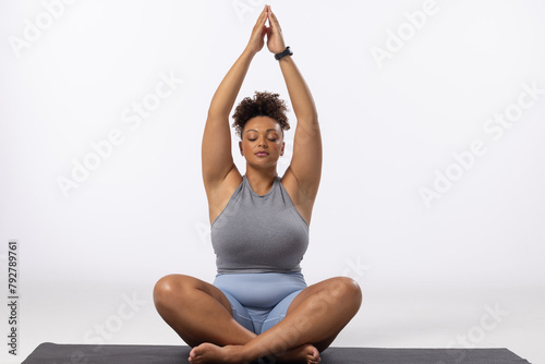 Biracial plus size model practices yoga on white background, copy space